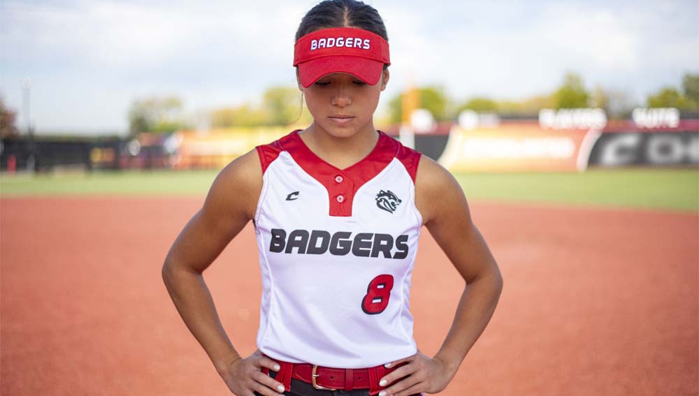 Teen girl softball player in infield wearing branded hat and jersey.